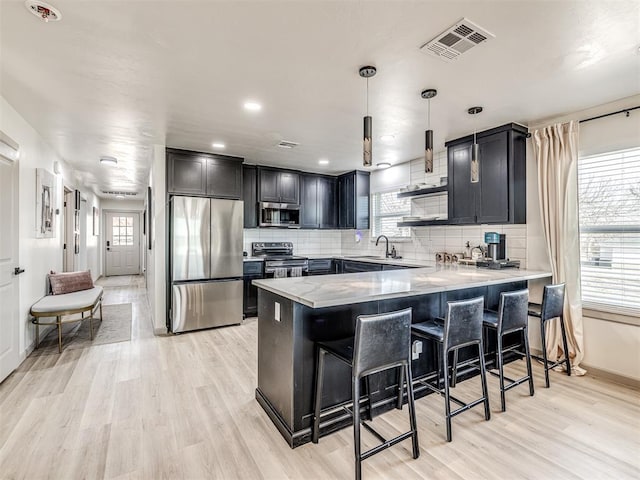 kitchen featuring appliances with stainless steel finishes, decorative light fixtures, sink, kitchen peninsula, and light wood-type flooring