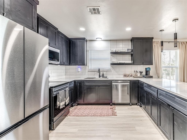 kitchen featuring pendant lighting, backsplash, light hardwood / wood-style floors, and appliances with stainless steel finishes