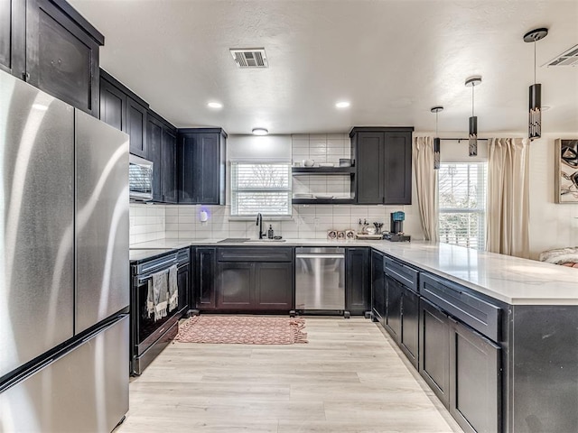 kitchen with pendant lighting, backsplash, stainless steel appliances, and light hardwood / wood-style floors