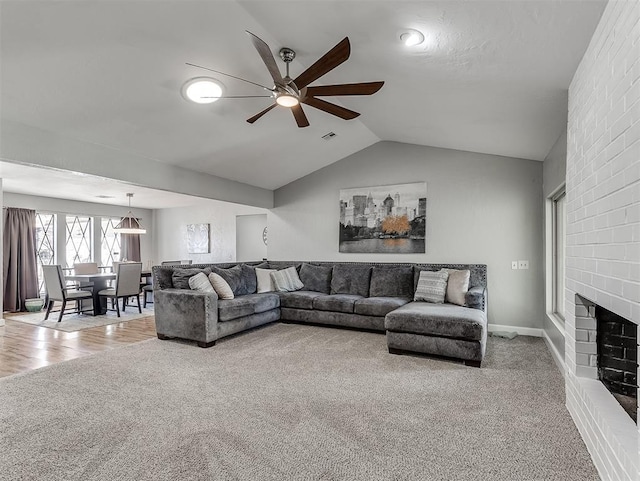 carpeted living room with ceiling fan, vaulted ceiling, and a fireplace