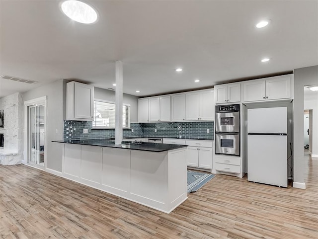 kitchen featuring stainless steel double oven, white fridge, white cabinets, light wood-type flooring, and kitchen peninsula