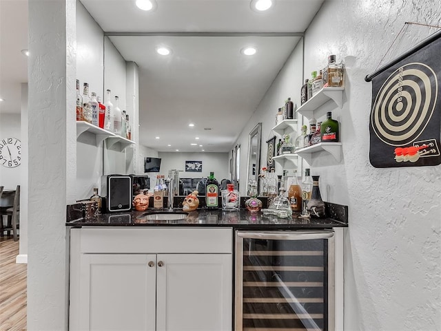 bar with white cabinetry, dark stone countertops, wine cooler, sink, and light wood-type flooring