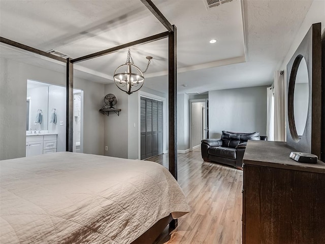 bedroom with light hardwood / wood-style floors, ensuite bath, and a tray ceiling