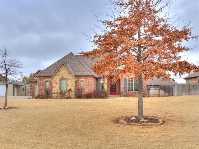 view of front of house with a shingled roof, a front yard, brick siding, and fence