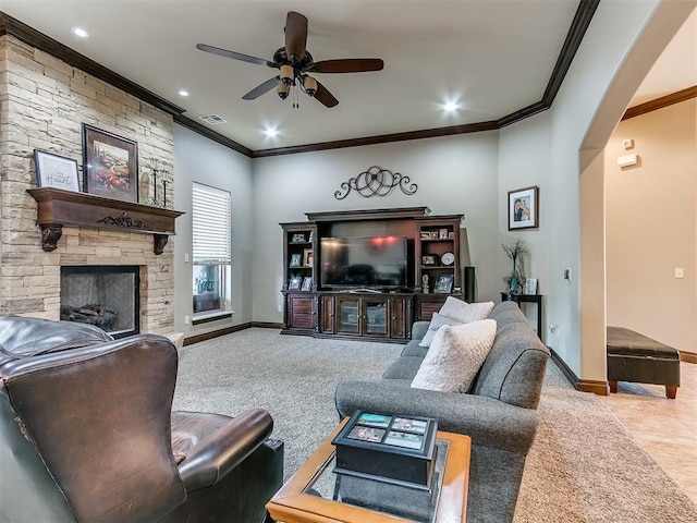 living room featuring arched walkways, a stone fireplace, a ceiling fan, visible vents, and baseboards