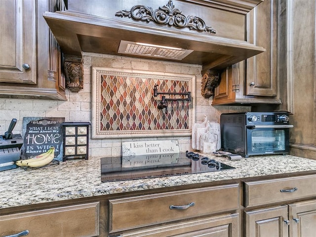 kitchen with a toaster, decorative backsplash, custom range hood, light stone countertops, and black electric stovetop