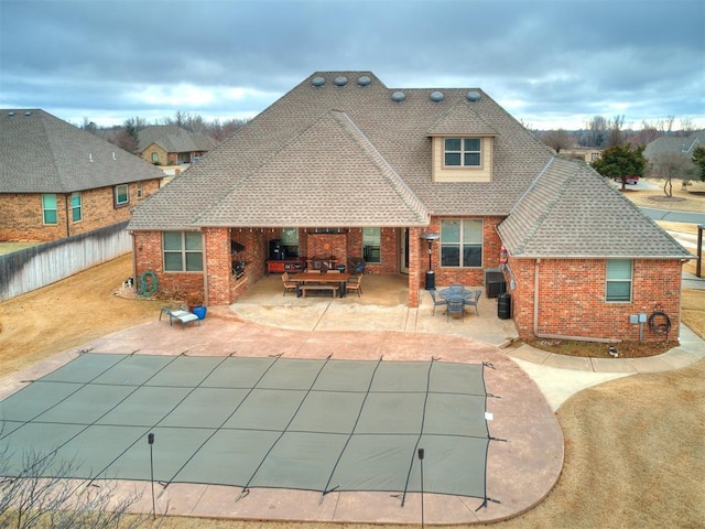 rear view of house featuring a covered pool, fence, brick siding, and a patio