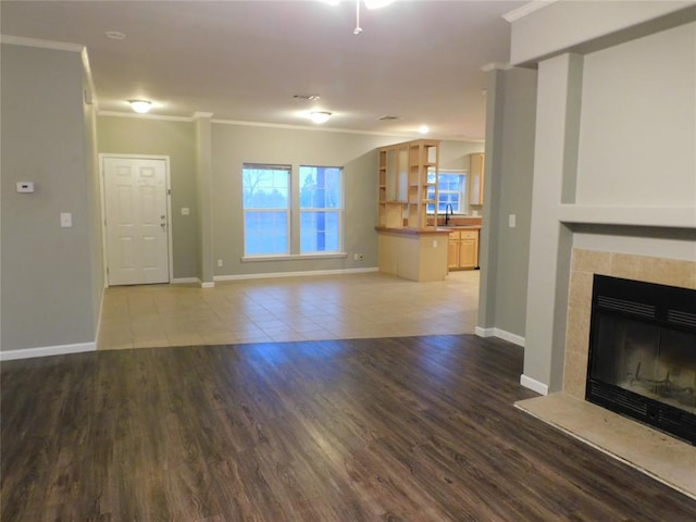 unfurnished living room with a tiled fireplace, ornamental molding, hardwood / wood-style flooring, and sink