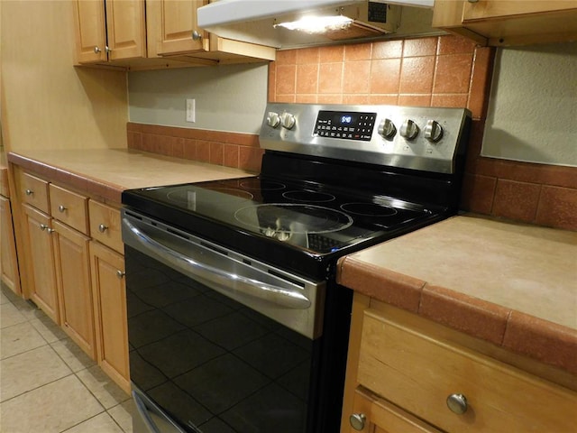 kitchen with stainless steel electric stove, decorative backsplash, light tile patterned floors, and tile countertops