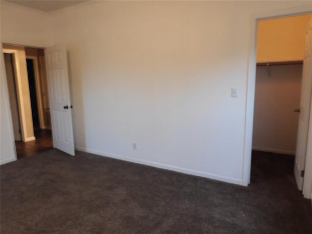 unfurnished bedroom featuring a closet, a spacious closet, and dark carpet