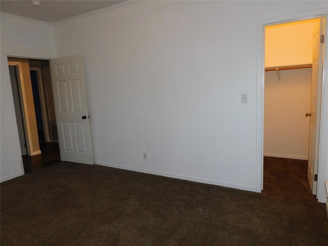 unfurnished bedroom featuring dark carpet, crown molding, a closet, and a walk in closet