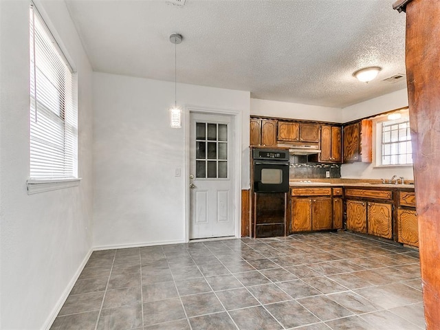 kitchen with pendant lighting, black oven, sink, backsplash, and a textured ceiling