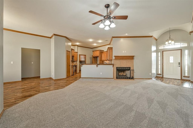 unfurnished living room featuring light carpet, ceiling fan with notable chandelier, a fireplace, and ornamental molding