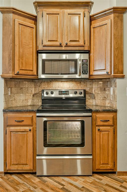 kitchen with tasteful backsplash, light hardwood / wood-style flooring, stainless steel appliances, and dark stone counters