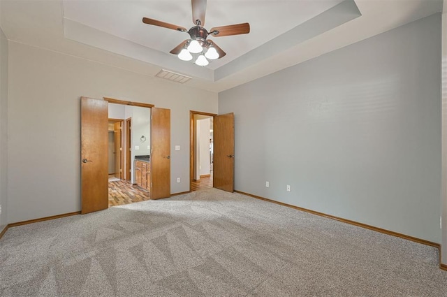 unfurnished bedroom with light colored carpet, ceiling fan, and a tray ceiling