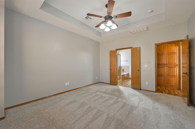 unfurnished bedroom with light colored carpet, a raised ceiling, ceiling fan, and ensuite bathroom