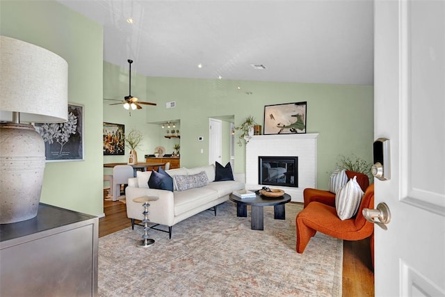 living area featuring wood finished floors, visible vents, high vaulted ceiling, a fireplace, and ceiling fan