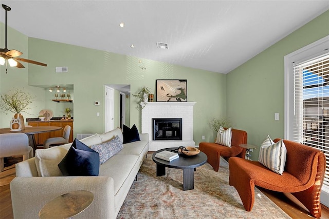 living room featuring visible vents, wood finished floors, a brick fireplace, ceiling fan, and vaulted ceiling