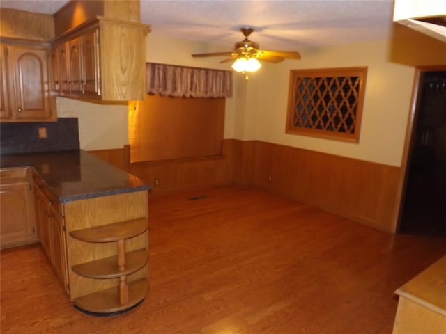 kitchen featuring ceiling fan, light wood-type flooring, and wood walls