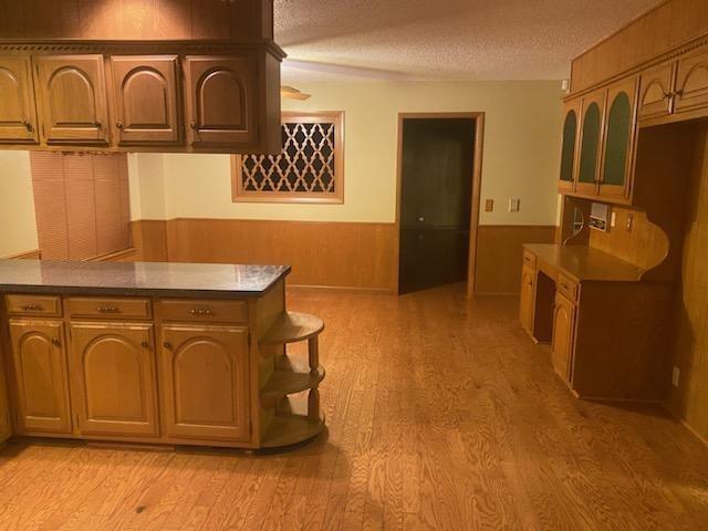 kitchen featuring light hardwood / wood-style floors, kitchen peninsula, a textured ceiling, and wood walls