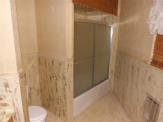 bathroom featuring bath / shower combo with glass door, tile walls, and toilet