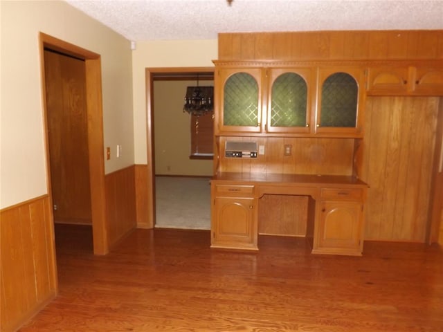 kitchen featuring a textured ceiling, hanging light fixtures, light hardwood / wood-style floors, and wooden walls