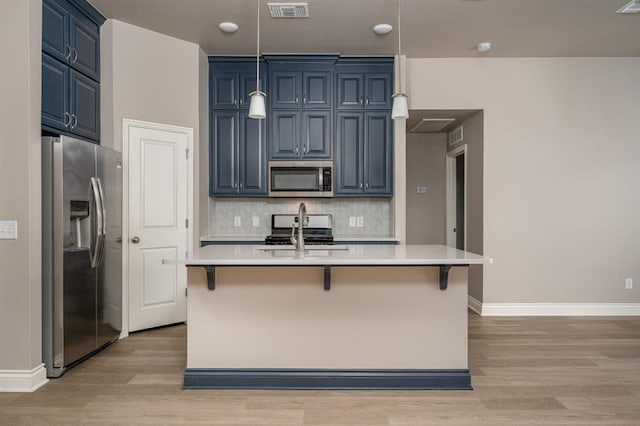 kitchen featuring blue cabinetry, appliances with stainless steel finishes, a center island with sink, and a breakfast bar area