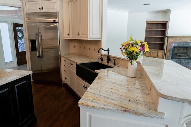 kitchen with tasteful backsplash, light stone countertops, sink, and built in fridge