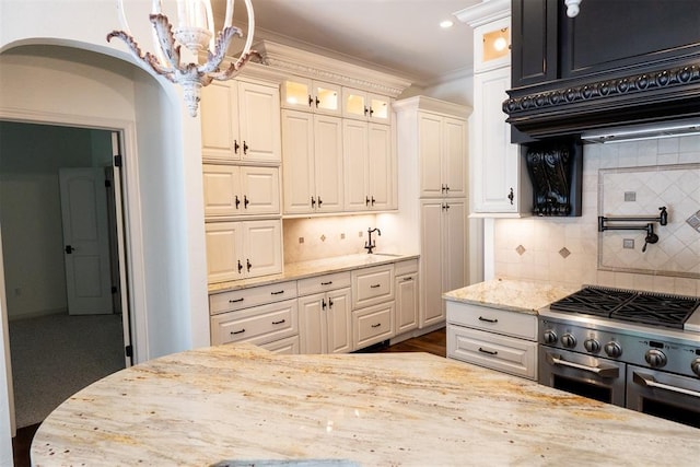 kitchen featuring light stone countertops, ornamental molding, tasteful backsplash, and high end stove