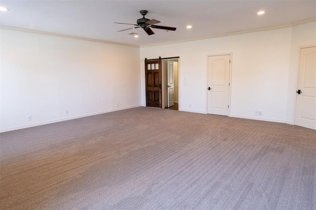 carpeted empty room featuring ceiling fan, crown molding, and a barn door