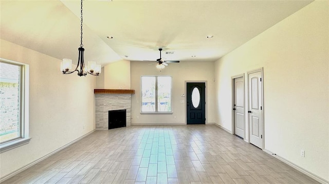 unfurnished living room featuring ceiling fan with notable chandelier, a tile fireplace, and a healthy amount of sunlight