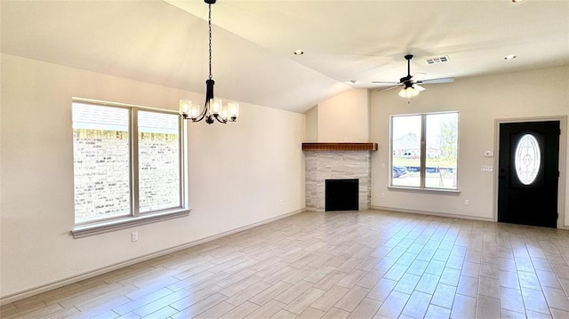 unfurnished living room with ceiling fan with notable chandelier, a wealth of natural light, lofted ceiling, and a fireplace