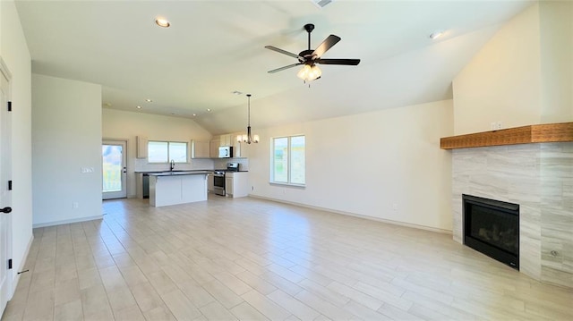 unfurnished living room featuring lofted ceiling, a fireplace, sink, light hardwood / wood-style flooring, and ceiling fan with notable chandelier