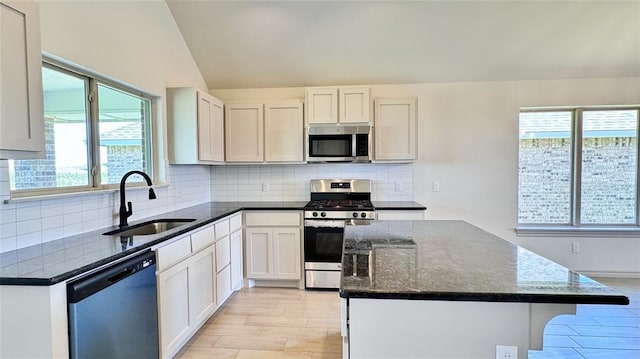 kitchen with lofted ceiling, dark stone countertops, sink, white cabinetry, and appliances with stainless steel finishes