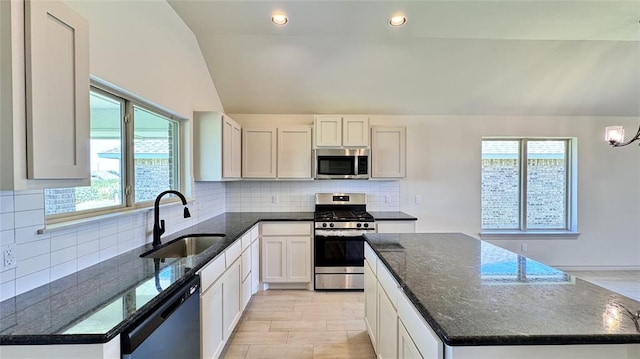 kitchen with stainless steel appliances, dark stone counters, vaulted ceiling, white cabinets, and sink