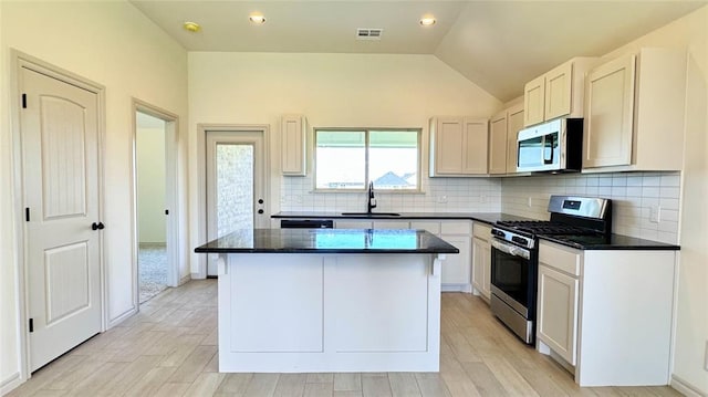 kitchen with lofted ceiling, appliances with stainless steel finishes, white cabinetry, and a center island