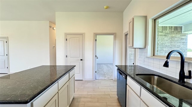 kitchen featuring sink, backsplash, white cabinets, and dark stone countertops