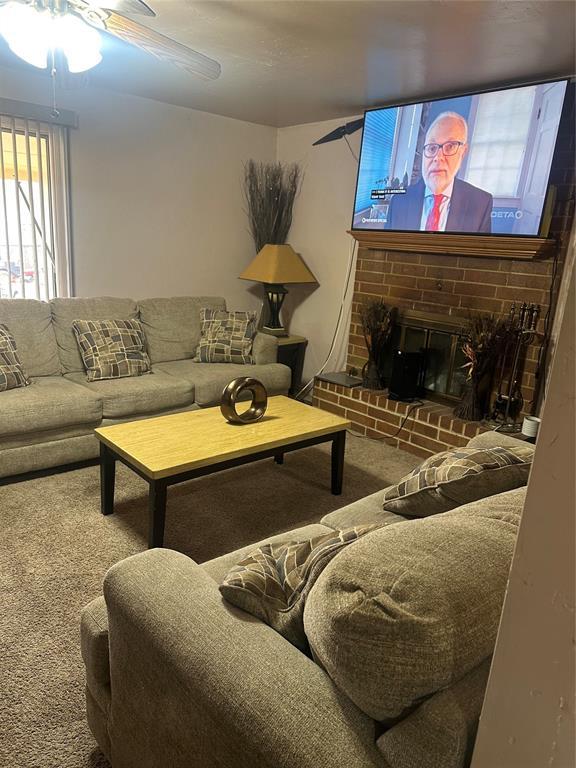 carpeted living room with ceiling fan and a brick fireplace