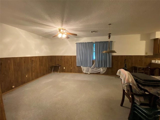 carpeted dining space featuring wooden walls, a wainscoted wall, ceiling fan, and a textured ceiling