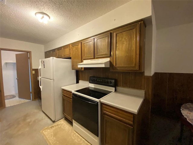 kitchen featuring range with electric cooktop, under cabinet range hood, freestanding refrigerator, a wainscoted wall, and a textured ceiling
