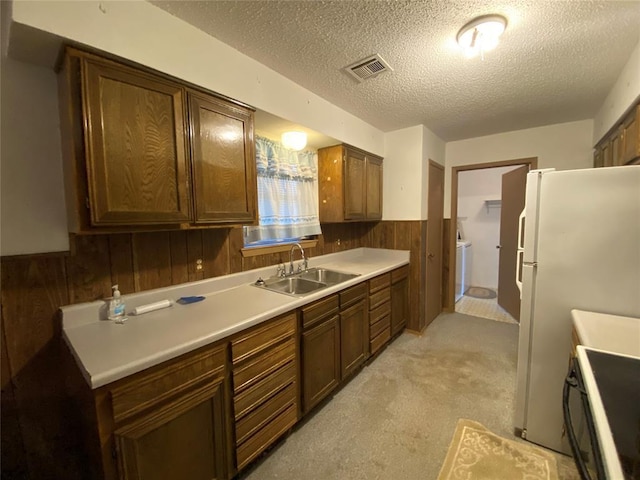 kitchen featuring a sink, a textured ceiling, range, wooden walls, and a wainscoted wall