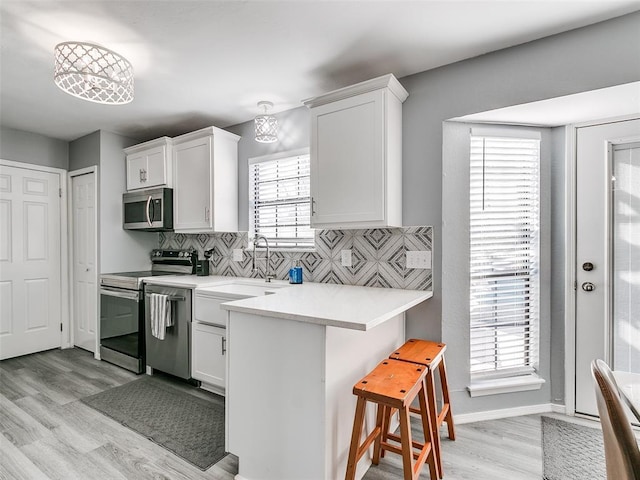 kitchen featuring a kitchen bar, appliances with stainless steel finishes, white cabinetry, decorative backsplash, and sink