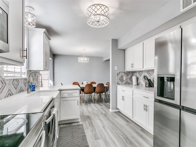 kitchen with appliances with stainless steel finishes, decorative light fixtures, backsplash, white cabinets, and a chandelier