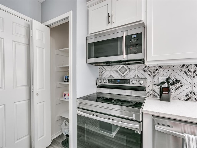 kitchen with appliances with stainless steel finishes, hardwood / wood-style flooring, decorative backsplash, white cabinets, and light stone counters