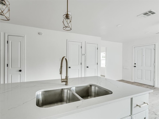 kitchen with sink, decorative light fixtures, white cabinetry, and light stone countertops