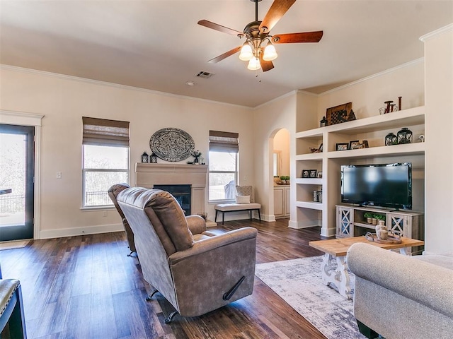 living room with ceiling fan, built in shelves, dark hardwood / wood-style flooring, and crown molding