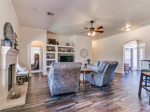 living room featuring built in shelves, crown molding, ceiling fan, and dark hardwood / wood-style flooring