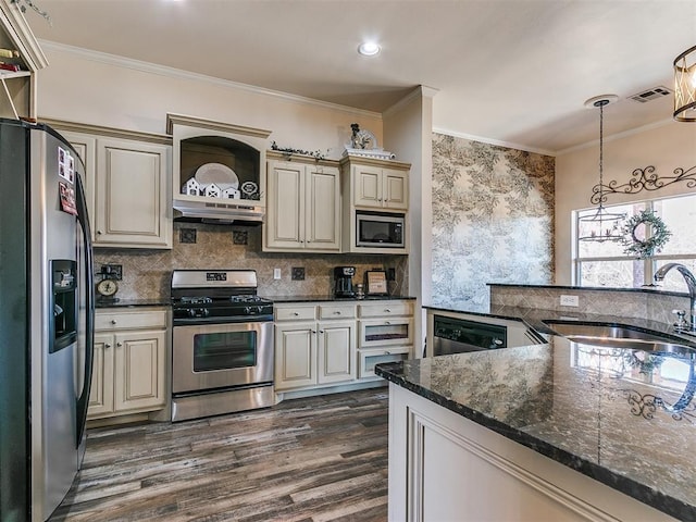 kitchen with sink, dark stone countertops, cream cabinetry, pendant lighting, and stainless steel appliances