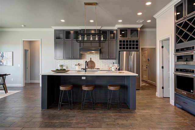 kitchen featuring sink, decorative light fixtures, ornamental molding, stainless steel appliances, and a center island with sink