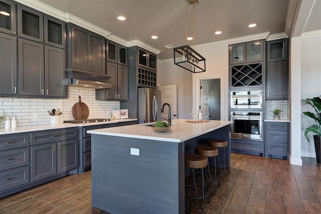 kitchen with dark hardwood / wood-style flooring, sink, a kitchen island with sink, decorative backsplash, and stainless steel appliances